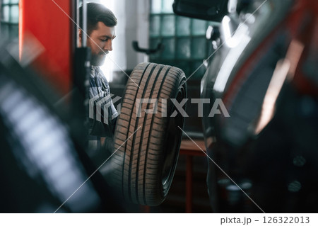 Changing the tire of the car. Man in uniform is working in the auto salon 126322013