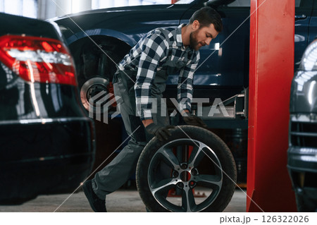 Side view. Moving the tire for the car. Man in uniform is working in the auto salon Side view. Moving the tire for the car. Man in uniform is working in the auto salon 126322026