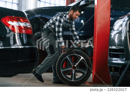 Side view. Moving the tire for the car. Man in uniform is working in the auto salon Side view. Moving the tire for the car. Man in uniform is working in the auto salon 126322027