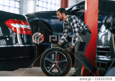 Side view. Moving the tire for the car. Man in uniform is working in the auto salon Side view. Moving the tire for the car. Man in uniform is working in the auto salon 126322029