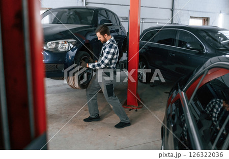 Front left wheel is changing. Man in uniform is working in the auto salon 126322036