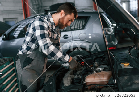 Mechanic is using a tool to repair the car under the hood. Man in uniform is working in the auto salon Mechanic is using a tool to repair the car under the hood. Man in uniform is working in the auto salon 126322053