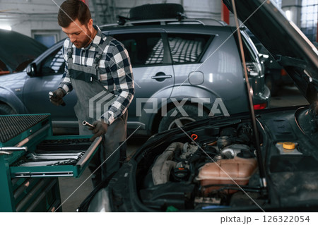 Choosing the tools. Man in uniform is working in the auto salon 126322054