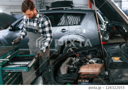 Choosing the tools. Man in uniform is working in the auto salon Choosing the tools. Man in uniform is working in the auto salon 126322055