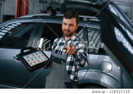 Showing gesture and smiling. Holding tablet. Man in uniform is working in the auto salon 126322138