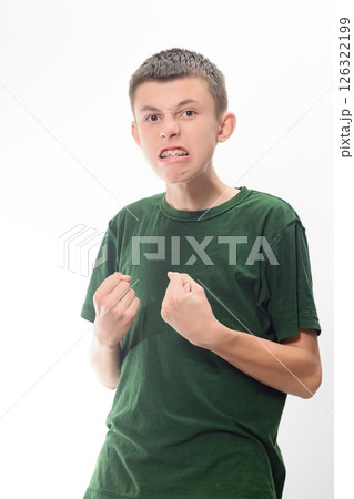 Angry teenage boy clenching fists, wearing a green shirt. Studio shot against a white background. 126322199