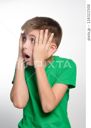 Surprised boy in green shirt. Hands on face, looking shocked. Youthful expression of amazement. 126322508