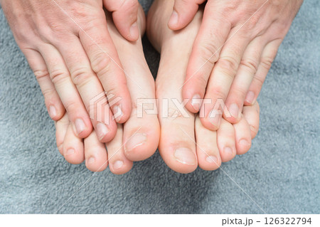 Close-up of hands holding feet on a soft gray surface. 126322794