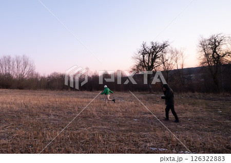 Joyful children playing in an open field during the twilight hours surrounded by trees with a serene landscape at dusk near a quiet village 126322883