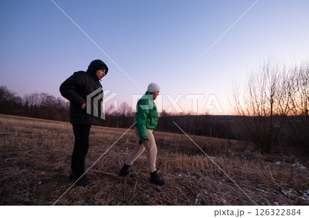 Two friends explore a serene field at dusk, wrapped in warm layers as day transitions to night, enjoying the peaceful landscape and fading light of winter 126322884