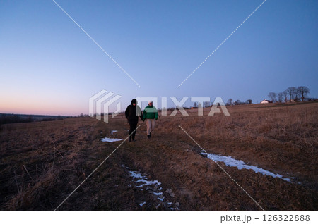 Couples stroll across a serene meadow at dusk, hand in hand, as the soft glow of twilight embraces the quiet landscape in winter 126322888