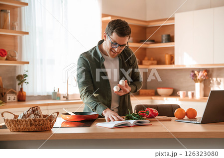 Holding two eggs in hand. Handsome man is on the kitchen at daytime 126323080