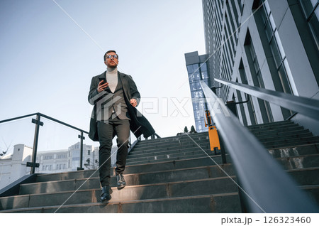 On the stairs. Handsome man in formal clothes is outdoor near the business building 126323460