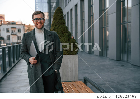 Smiling, feeling good. Handsome man in formal clothes is outdoor near the business building 126323468
