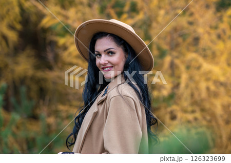 Beautiful brunette girl in beige coat and hat posing in autumn park Beautiful brunette girl in beige coat and hat posing in autumn park 126323699