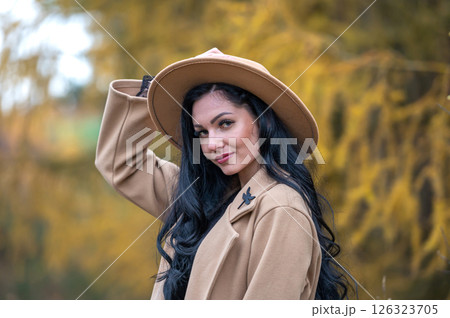 Beautiful brunette girl in beige coat and hat posing in autumn park 126323705
