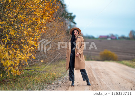 Portrait of a beautiful young brunette woman in coat and hat on a country road Portrait of a beautiful young brunette woman in coat and hat on a country road 126323711