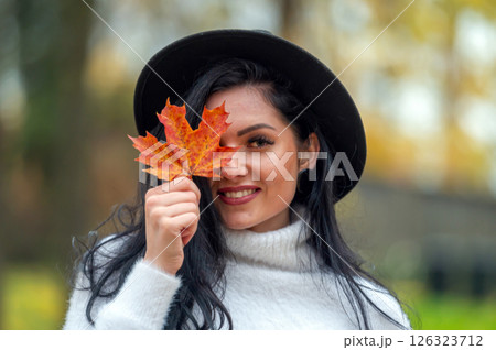 Portrait of a beautiful young woman in the autumn park with maple leaf 126323712