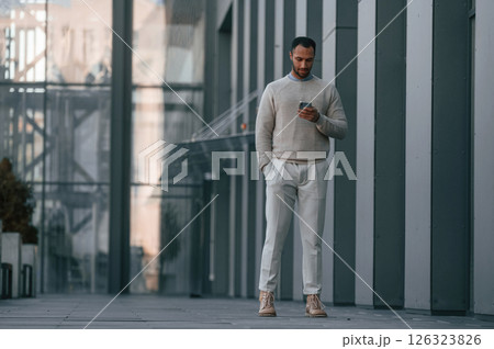 Handsome man is walking, holding smartphone. Outdoors near the business building 126323826