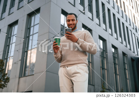 Against modern business building. With smarpthone. Handsome black man is outdoors 126324303