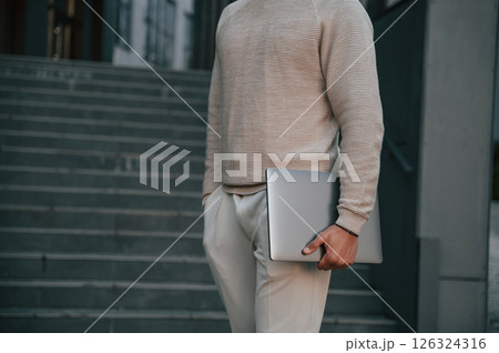 Close up view of man that is standing against the stairs outdoors and holding laptop 126324316