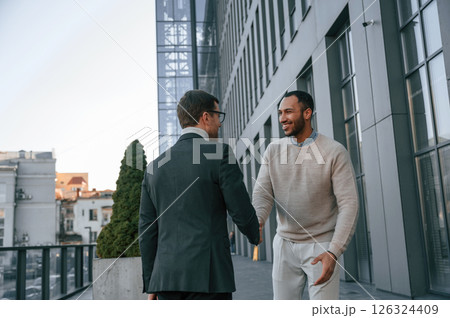 Conception of collaboration. Businessman in formal clothes is with black man outdoors in the city 126324409