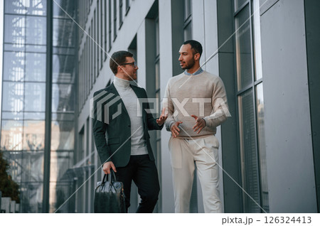 Walking together. Businessman in formal clothes is with black man outdoors in the city Walking together. Businessman in formal clothes is with black man outdoors in the city 126324413