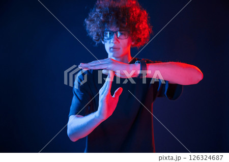 Hands gesture. Young man with curly hair is indoors illuminated by neon lighting 126324687