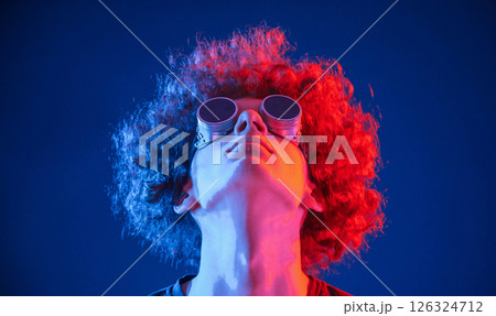 Portrait of young man with curly hair that is indoors illuminated by neon lighting. In retro eyewear 126324712