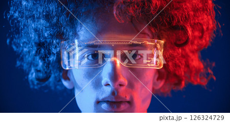 Close up view. In futuristic eyewear. Young man with curly hair is indoors illuminated by neon lighting 126324729