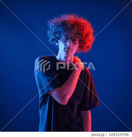Serious facial expression. Young man with curly hair is indoors illuminated by neon lighting Serious facial expression. Young man with curly hair is indoors illuminated by neon lighting 126324768