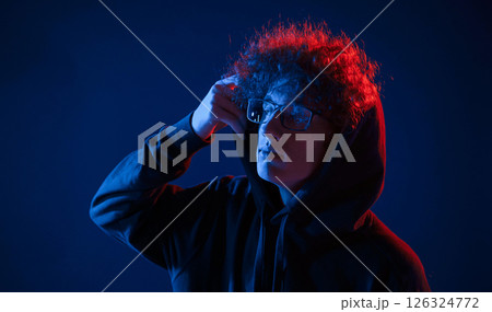 Wearing the hood. Young man with curly hair is indoors illuminated by neon lighting 126324772