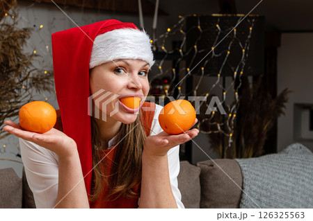 Joyous Holiday Celebration With a Young Woman Wearing a Santa Hat Holding Oranges 126325563