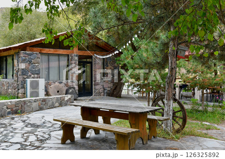 Scenic Outdoor Dining Area Next to Cozy Stone Cottage Surrounded by Trees in Nature 126325892