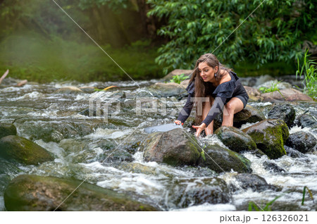 female freelancer sitting on a rock in the river and dropping her laptop into the water 126326021