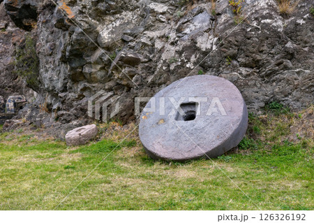 Ancient Stone Wheel and Smaller Artifact Beside Rocky Outcrop in Historical Site 126326192
