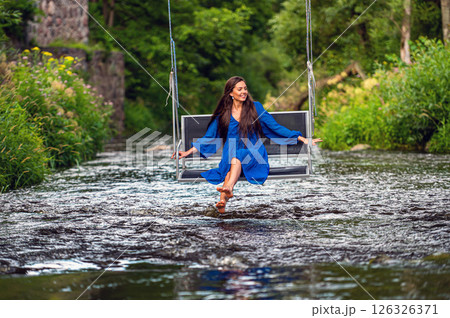 a joyful young woman swings on a rope swing across a fast-flowing river 126326371