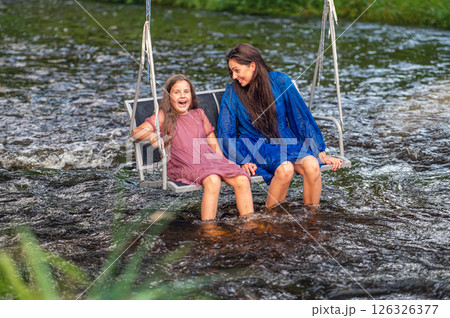 a woman and a young girl are swinging across a fast-flowing river, laughing and splashing with water 126326377