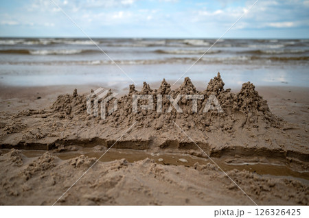 Sandcastle built on a beach with waves in the background during a cloudy day Sandcastle built on a beach with waves in the background during a cloudy day 126326425