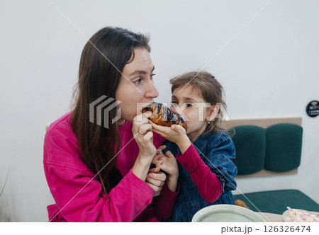 Mother and daughter in a cafe, drinking coffee and cocoa, eating a croissant and cake. Having fun and enjoying spending time together 126326474