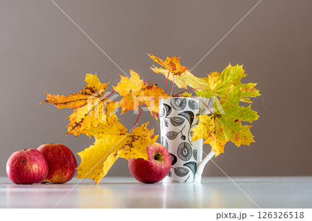 Apples and vibrant autumn leaves are arranged artistically on a simple tabletop. Apples and vibrant autumn leaves are arranged artistically on a simple tabletop. 126326518