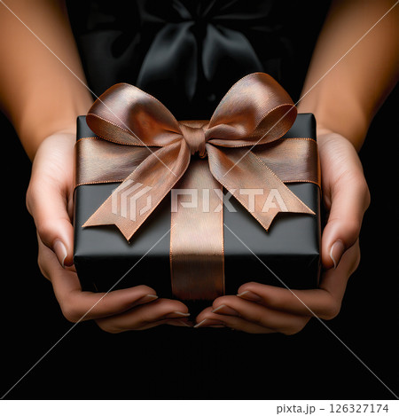 Elegant Black Gift Box with Gold Ribbon Held in Hands Against a Sophisticated Background 126327174
