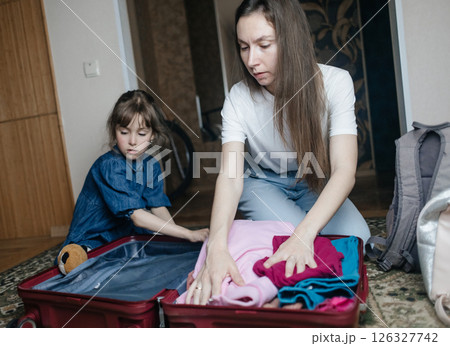 Tired mother with 6 year old daughter packing travel suitcase. Travel concept. Close-up of travel bag and tired faces of travelers. 126327742