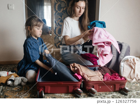 Tired mother with 6 year old daughter packing travel suitcase. Travel concept. Close-up of travel bag and tired faces of travelers. 126327756