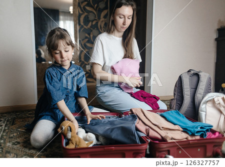 Tired mother with 6 year old daughter packing travel suitcase. Travel concept. Close-up of travel bag and tired faces of travelers. 126327757