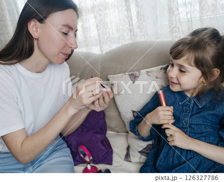 Mother putting makeup on her daughter face and they fool around together. Communication between women in the family. Fun time. Happy family concept. little girl doing her makeup 126327786