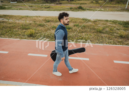Musician With Guitar Case Walking On The Sidewalk Near The Sea 126328005