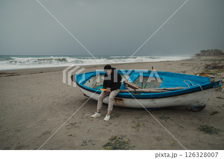 Man Reading A Book Sitting On The Beach In Winter Near A Boat Man Reading A Book Sitting On The Beach In Winter Near A Boat 126328007