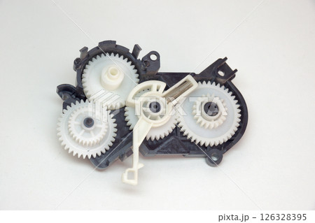 cogwheels mechanism in black plastic case. Part of inkjet printer: complex mechanical drive made of Multiple reducer gears of white plastic and spring 126328395