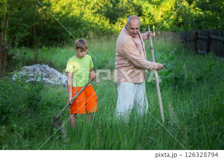 A man and a boy, father and son, work together in the field. They mow the grass. The scene represents collaboration and teamwork. 126328794